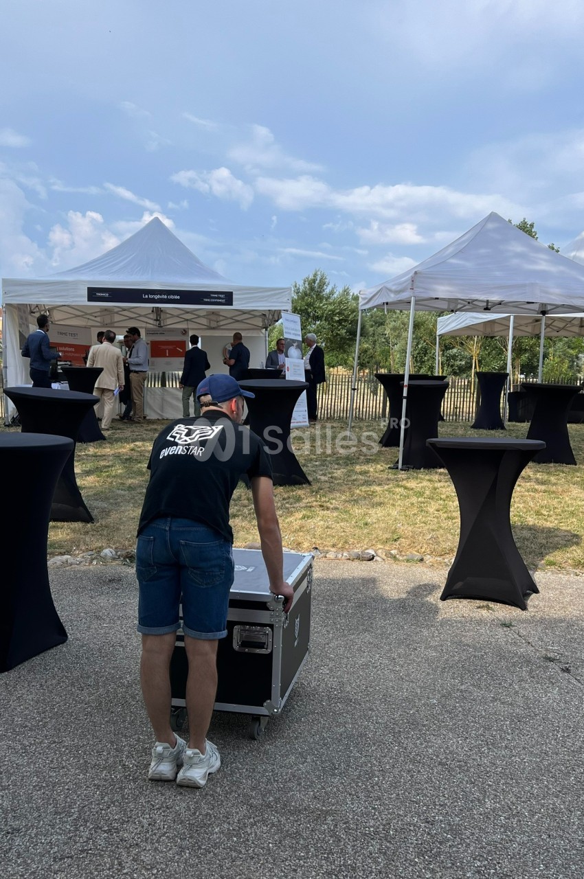 Un technicien déplace un caisson devant des tentes blanches lors d'un événement en extérieur.
