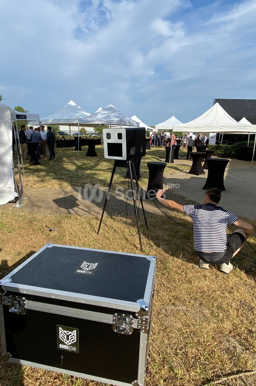 Un événement en extérieur avec des tentes blanches, un photobooth et un technicien ajustant un câble au sol.