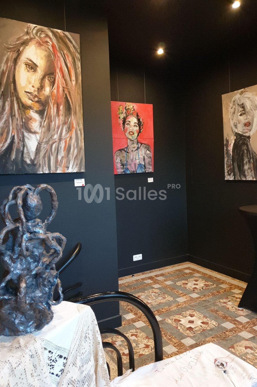 Exposition artistique dans une salle sombre avec des peintures de portraits colorés accrochées aux murs et une sculpture au…