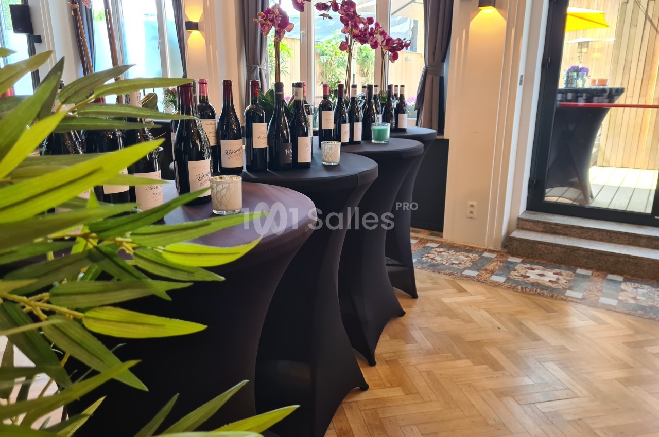 Bouteilles de vin disposées sur des tables hautes recouvertes de nappes noires, avec des orchidées en décoration.