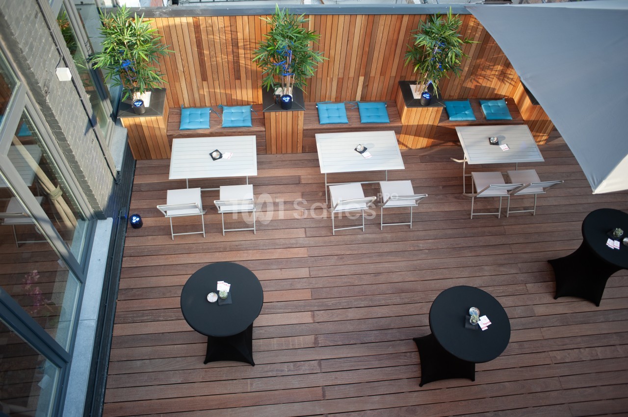Terrasse en bois aménagée avec tables, chaises, plantes et parasols, vue en hauteur.