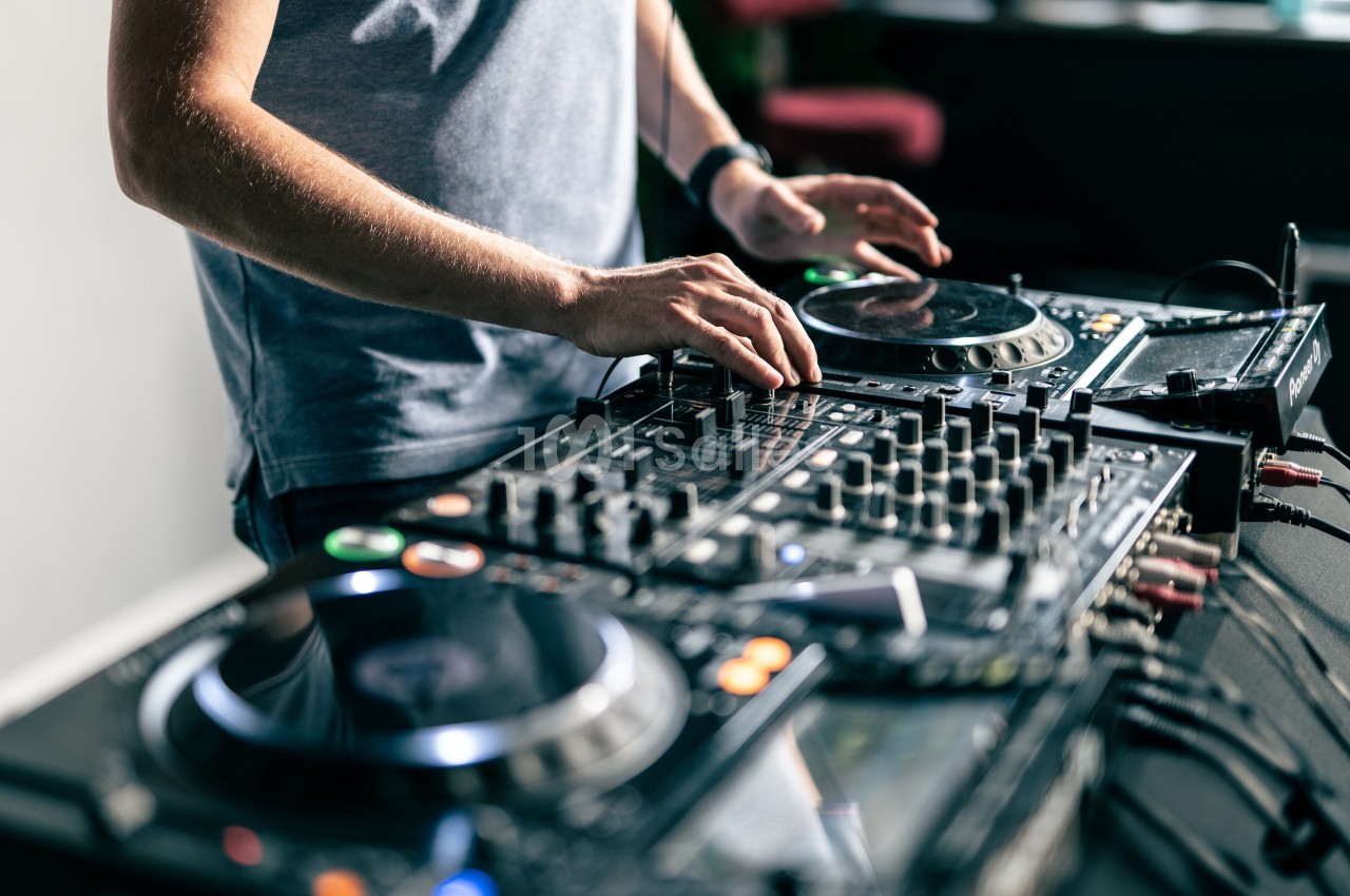 Un DJ mixant de la musique sur une table de mixage avec plusieurs platines et boutons.