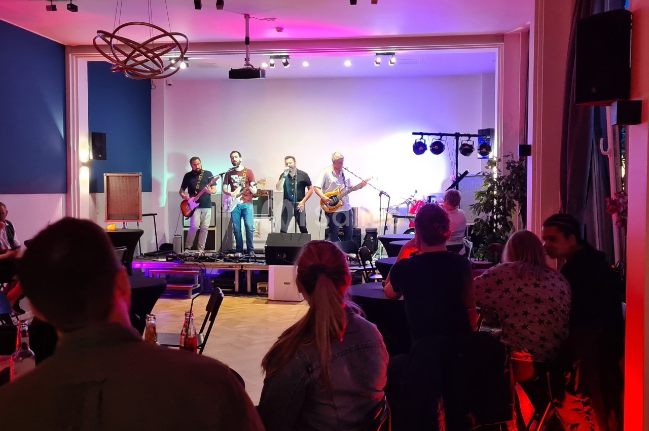 Un groupe de musiciens joue sur une scène éclairée, devant un public assis dans une salle.