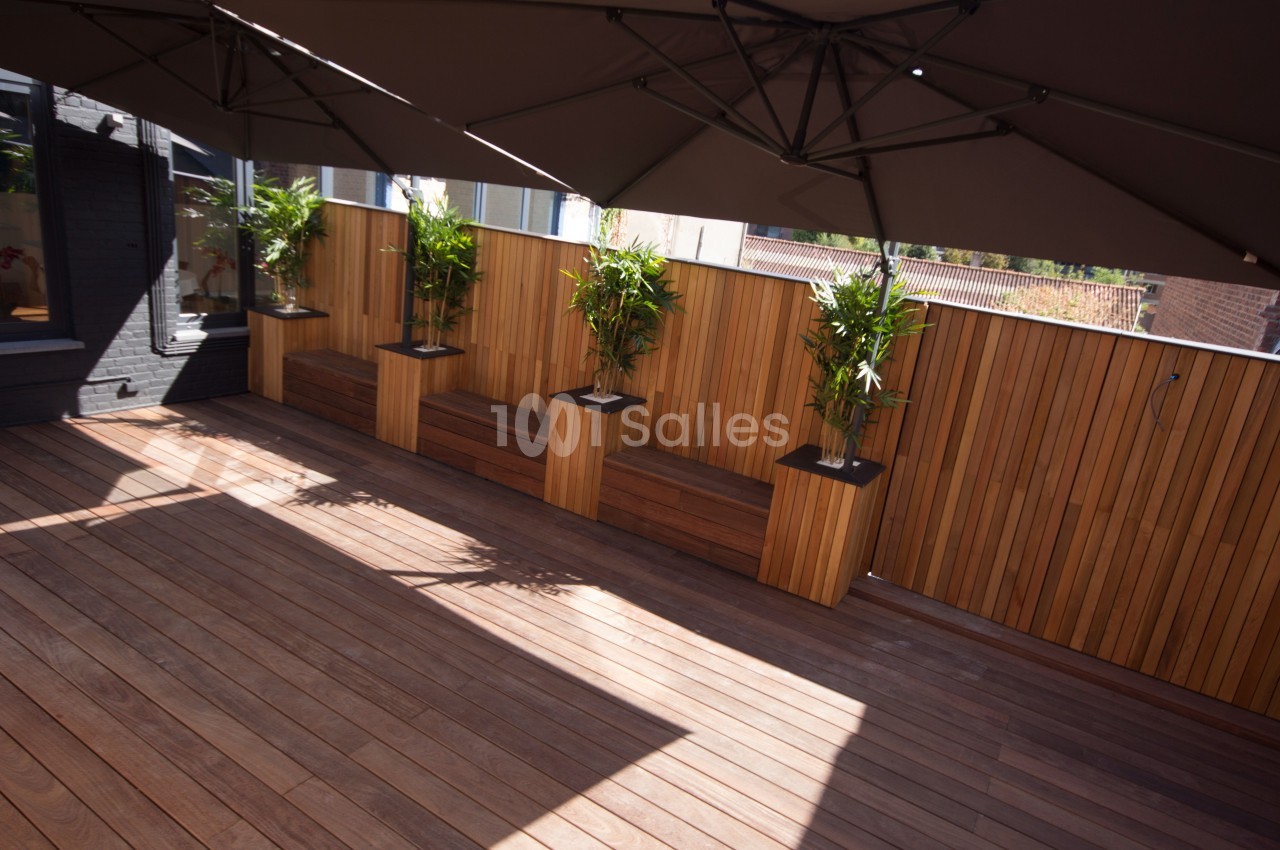 Terrasse en bois avec des bacs à plantes intégrés dans une clôture en bois, ombragée par de grands parasols.