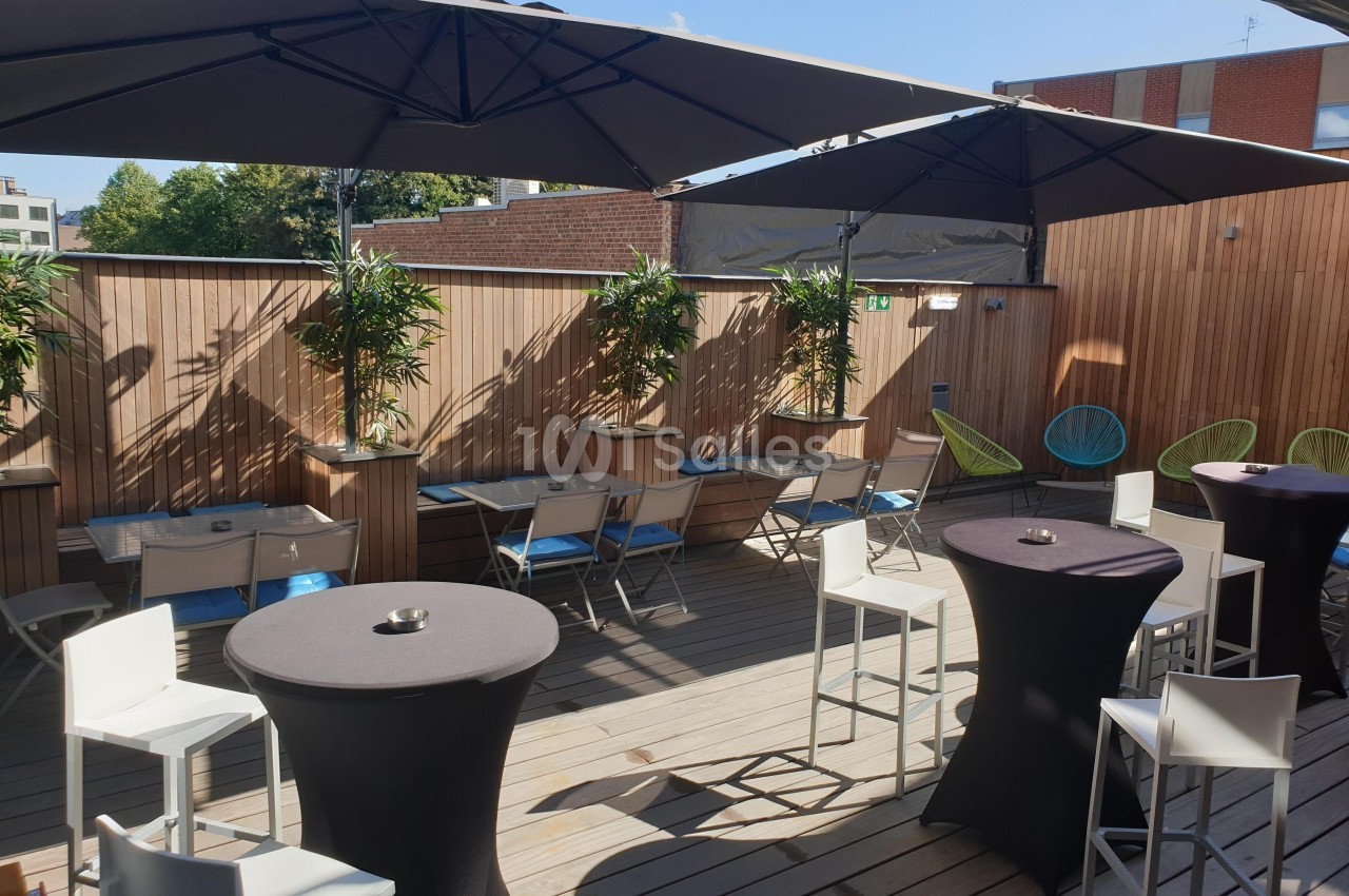 Terrasse en bois avec tables hautes et basses, chaises, parasols et plantes, entourée de murs en bois.