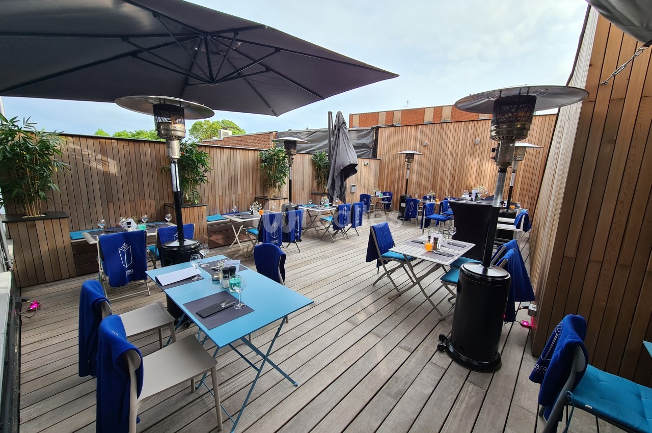 Terrasse en bois aménagée avec des tables et chaises bleues, parasols et chauffages extérieurs sous un ciel légèrement…