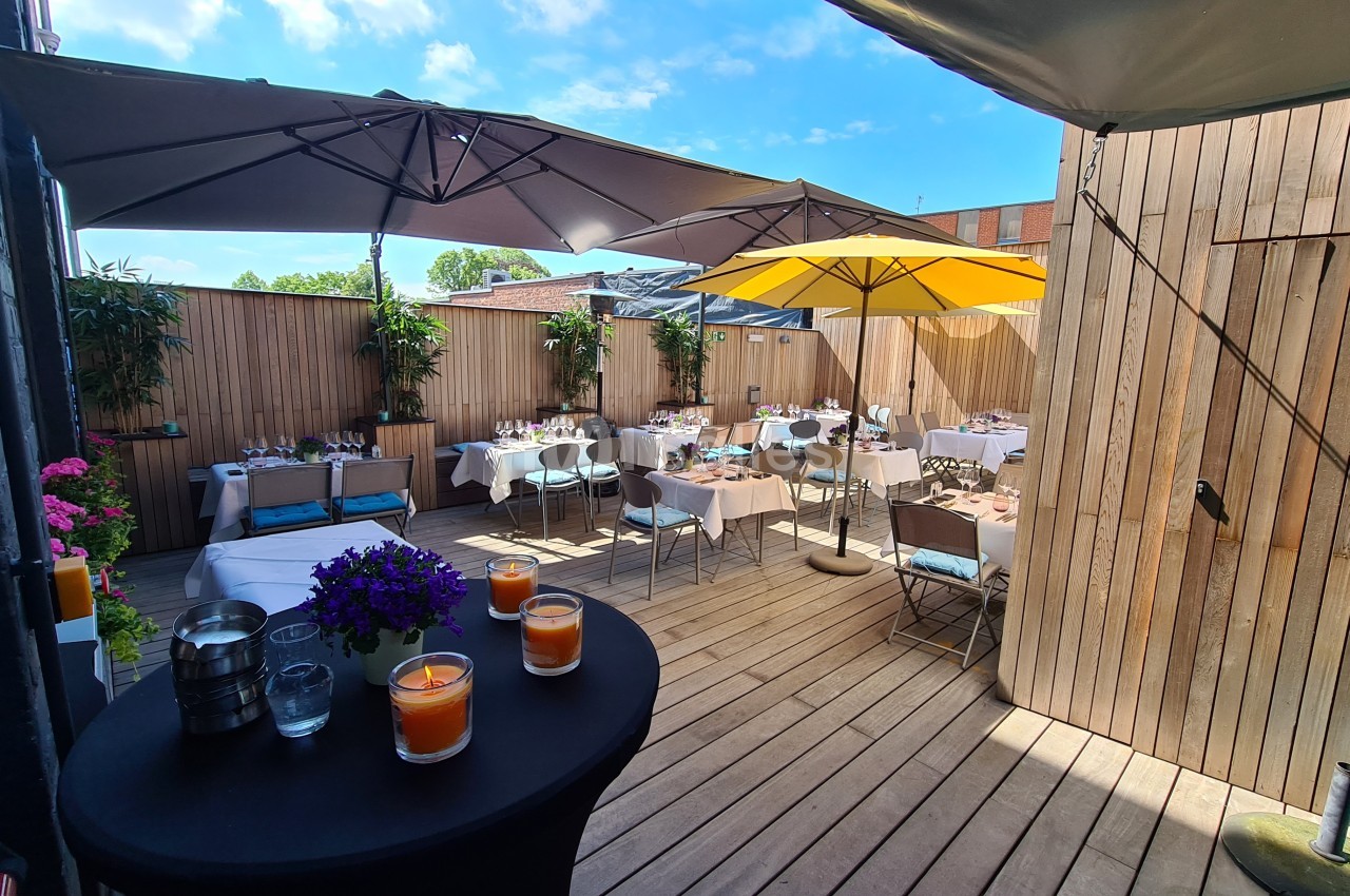 Terrasse en bois aménagée avec des tables dressées, des parasols et des plantes, sous un ciel partiellement dégagé.
