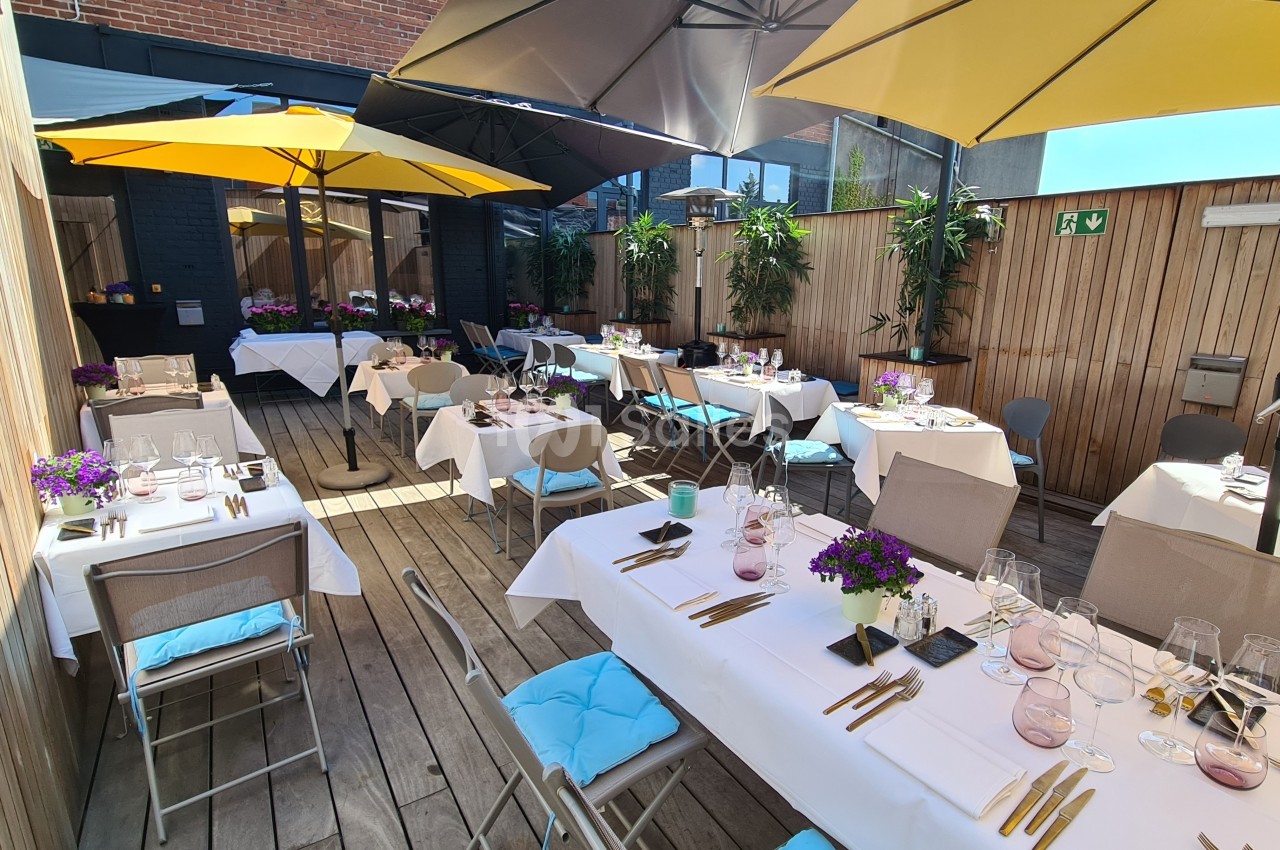 Terrasse aménagée avec des tables dressées, chaises colorées, parasols jaunes et plantes décoratives en fond.