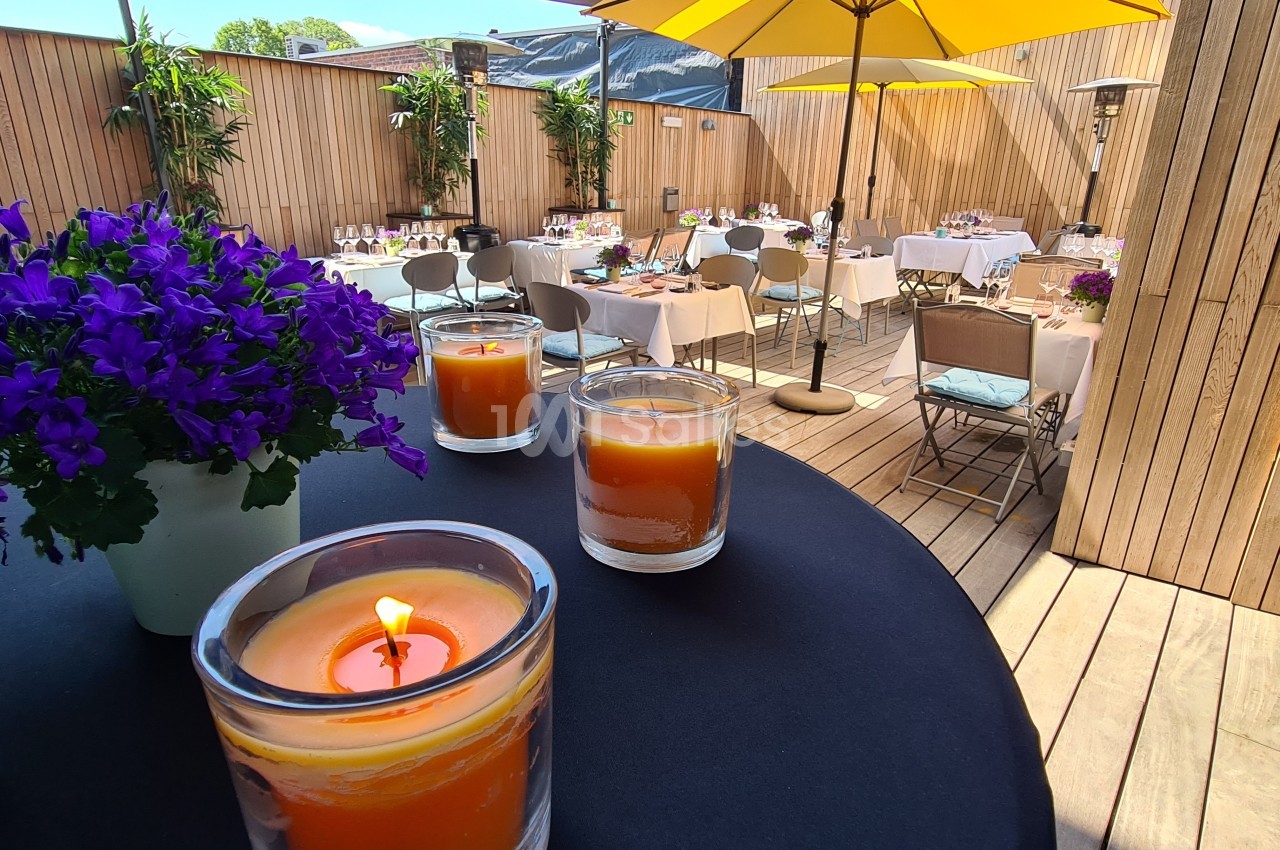 Terrasse en bois aménagée avec des tables dressées, des parasols jaunes et des bougies allumées sur une table.