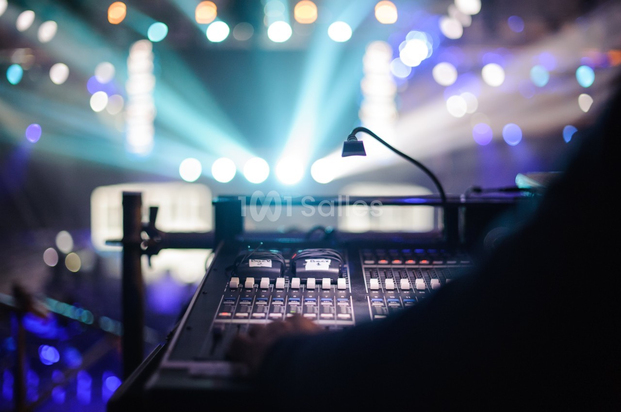 Table de mixage audio en gros plan avec des lumières de scène floues en arrière-plan.