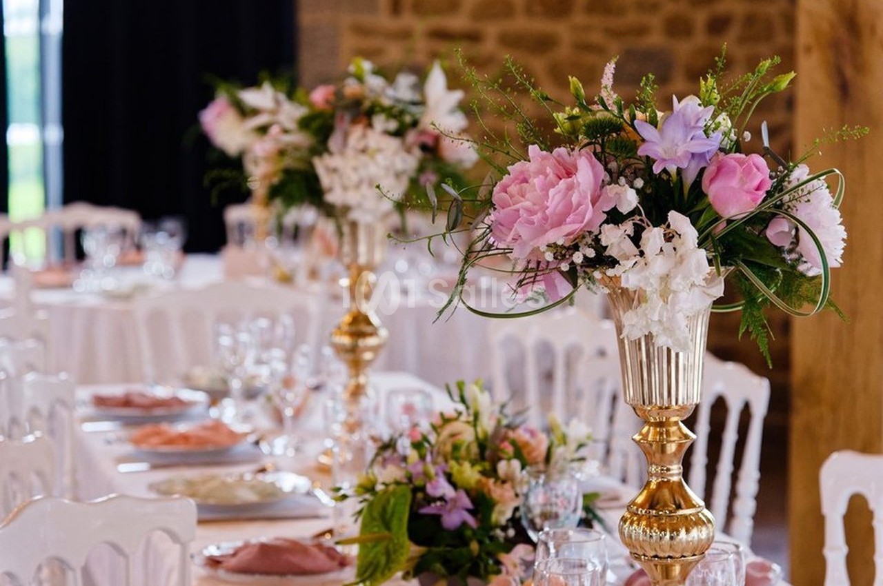 Centres de table fleuris avec des roses et pivoines dans des vases dorés, disposés sur des tables élégantes.