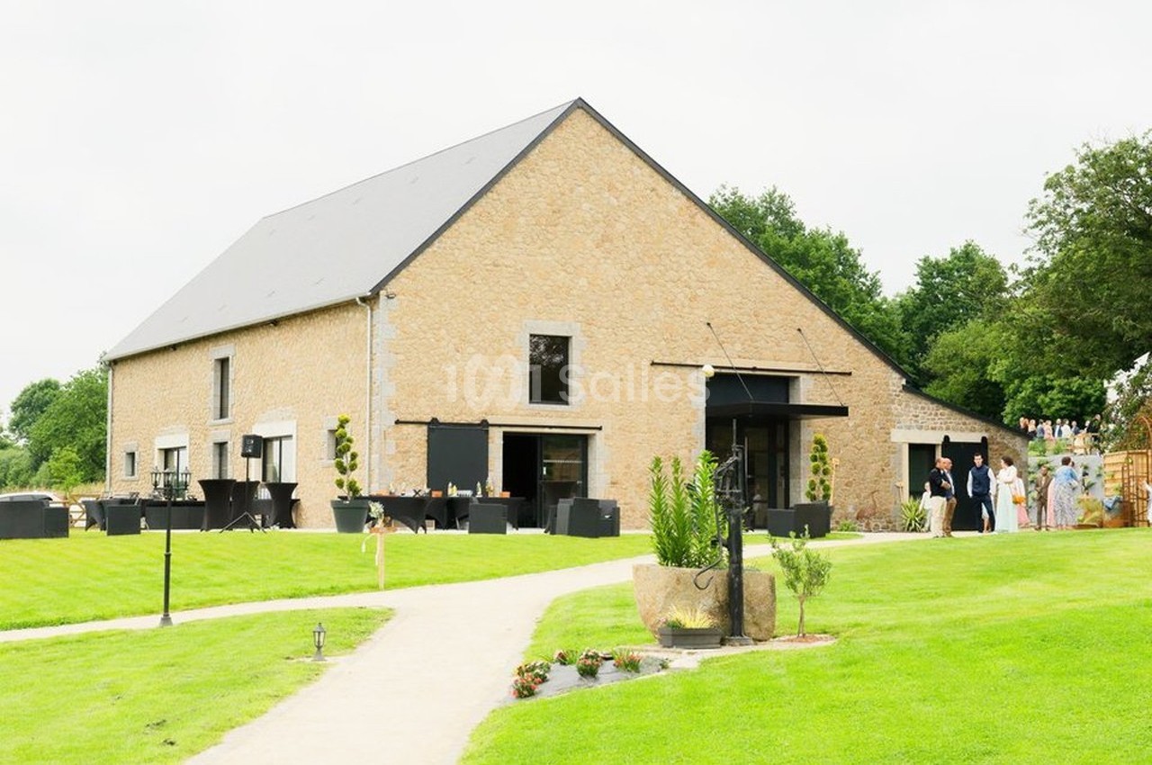 Bâtiment en pierre avec toit en ardoise, entouré de pelouses et d'arbres, avec des personnes à l'extérieur.