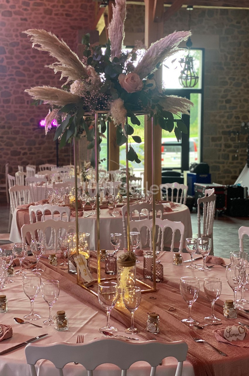 Salle de réception décorée avec des tables dressées, centre de table floral et nappes roses dans un cadre rustique.