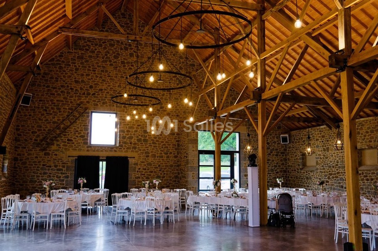 Salle de réception en pierre avec poutres apparentes, tables dressées et éclairage suspendu.