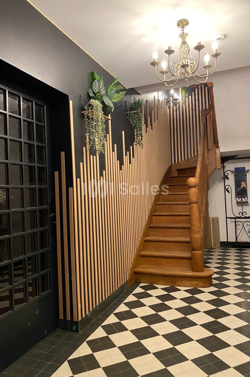 Escalier en bois avec rampe décorative, mur noir orné de plantes suspendues et sol en carrelage noir et blanc.