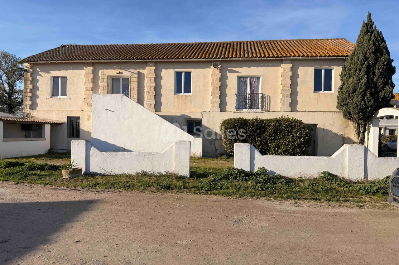 Grande maison de campagne à un étage avec façade beige, toit en tuiles et jardin clôturé devant.