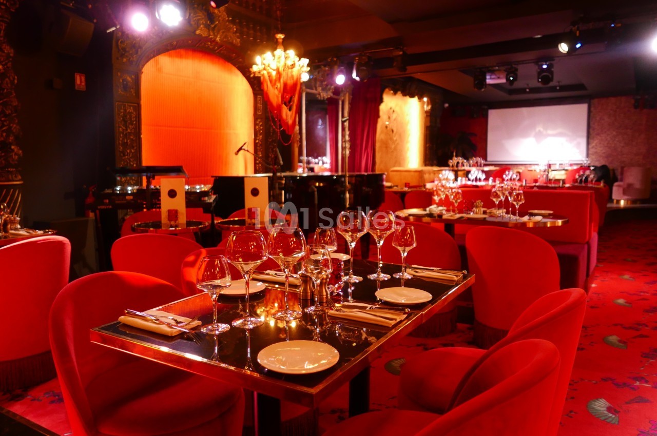 Salle de restaurant élégante avec tables dressées, chaises rouges, éclairage tamisé et décorations raffinées.