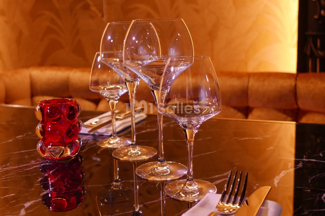 Quatre verres à vin alignés sur une table en marbre noir, avec un photophore rouge et des couverts à proximité.