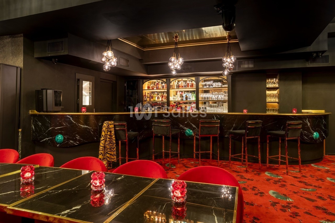 Bar élégant avec comptoir en marbre noir, tabourets hauts, éclairage tamisé et tables ornées de bougies rouges.
