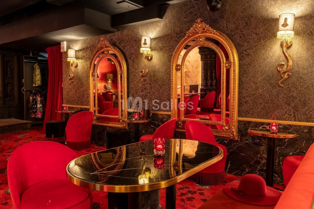 Salle élégante avec fauteuils rouges, tables en marbre noir, miroirs dorés et éclairage tamisé.