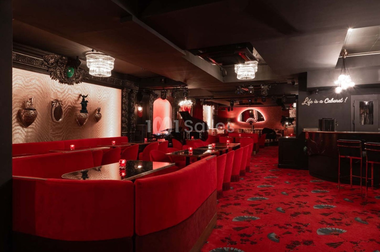 Salle de cabaret élégante avec banquettes rouges, lustres en cristal, piano et décorations murales sophistiquées.