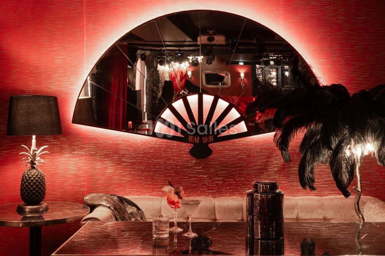 Salle décorée avec un éventail mural, éclairage rouge tamisé, table avec cocktails et objets décoratifs.