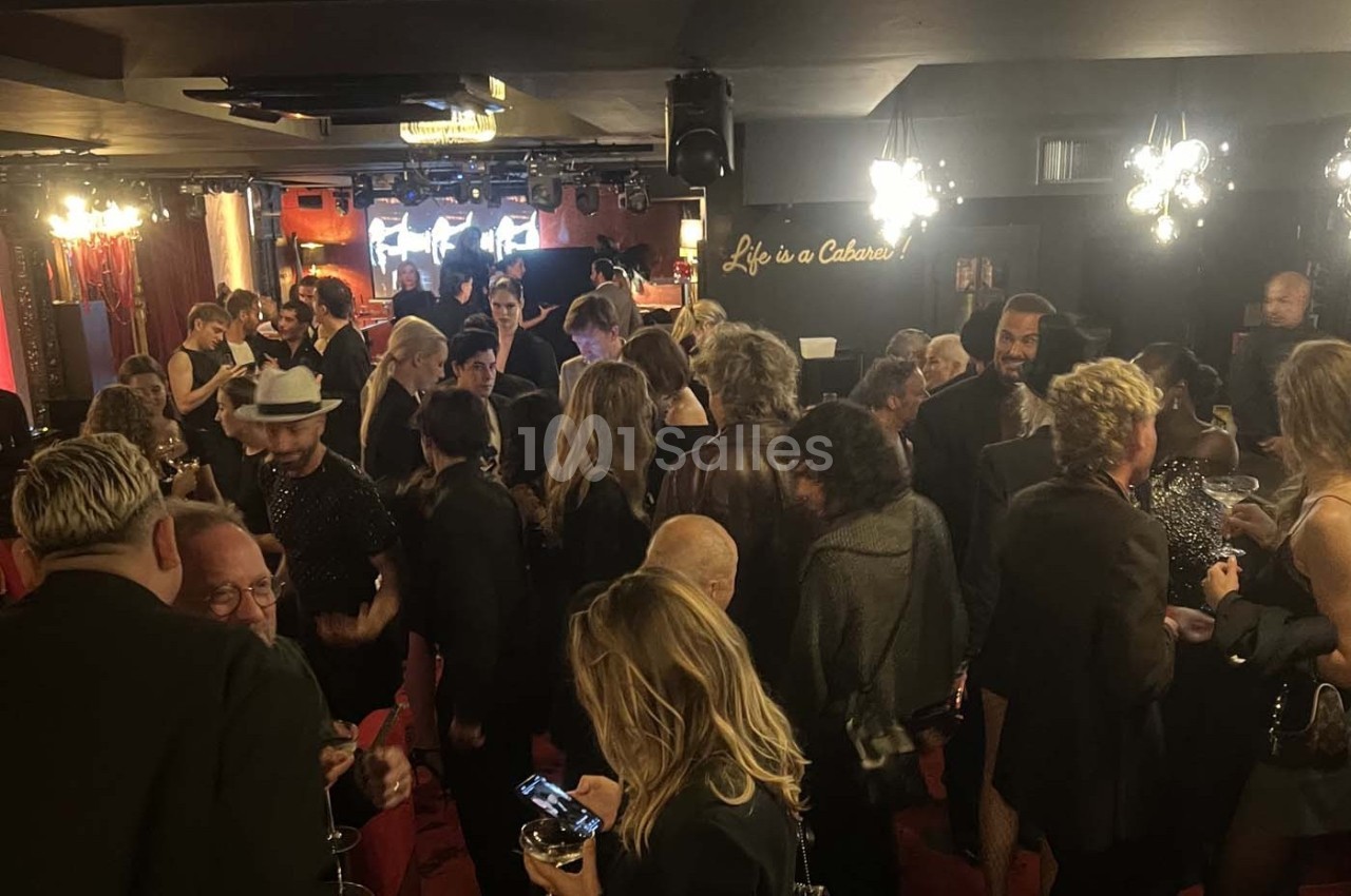 Groupe de personnes rassemblées dans un lieu animé avec une ambiance de cabaret et des lumières tamisées.