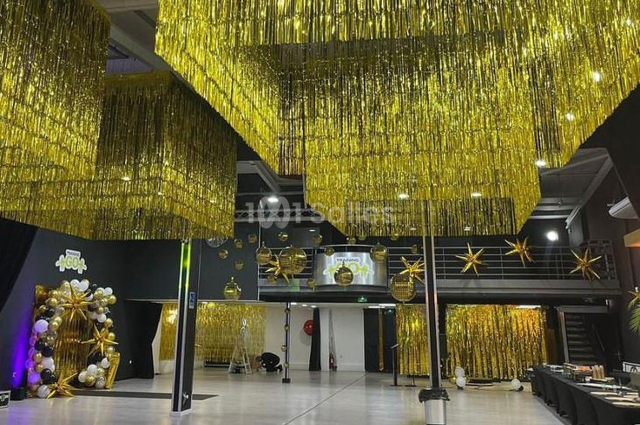 Salle décorée avec des guirlandes dorées suspendues, des ballons et des étoiles, prête pour un événement festif.
