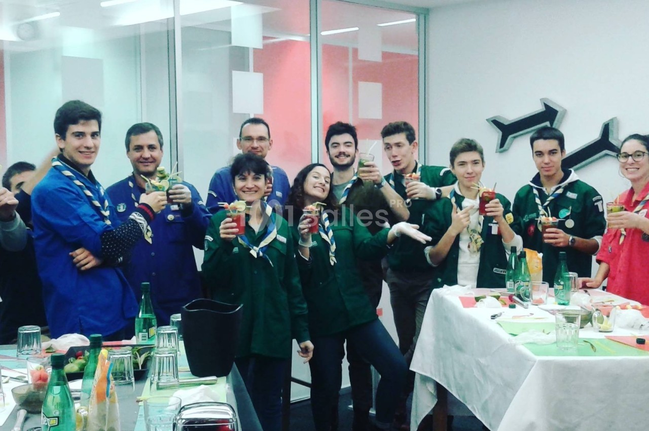 Un groupe de personnes en tenue de scouts partage un moment convivial autour de boissons dans une salle lumineuse.