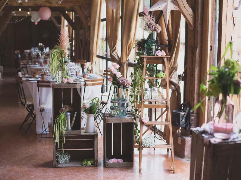 Décoration florale avec des plantes et fleurs sur des caisses en bois et une échelle dans une salle de réception lumineuse.