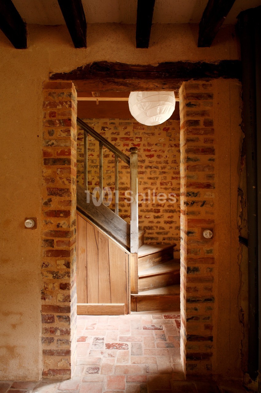 Vue d'un escalier en bois entouré de murs en briques dans une maison au style rustique.