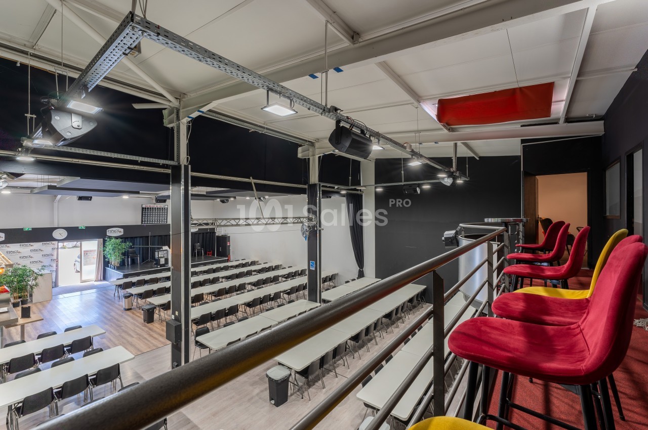 Salle de conférence avec tables alignées, vue depuis une mezzanine équipée de chaises rouges et jaunes.