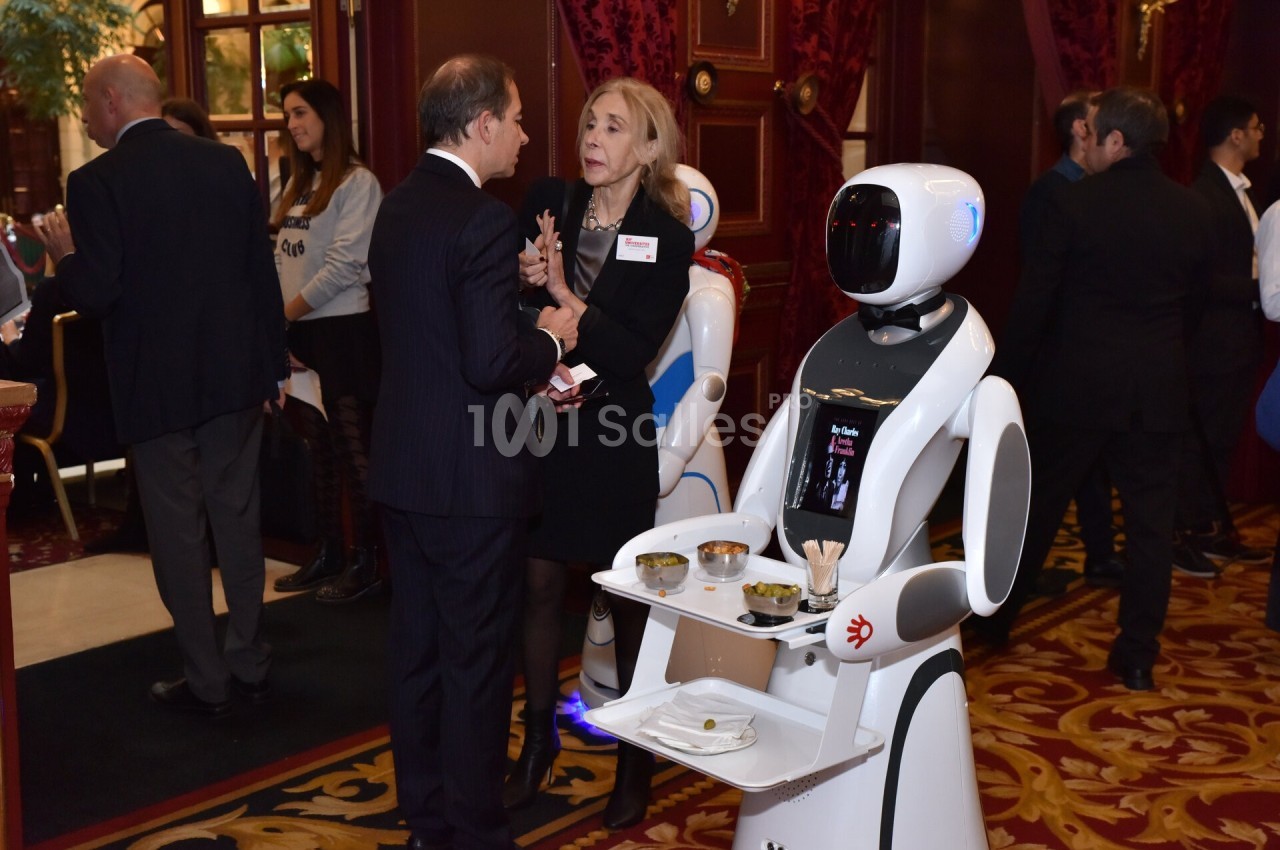 Un robot serveur transportant des plats dans un espace intérieur lors d'un événement avec plusieurs participants en arrière…