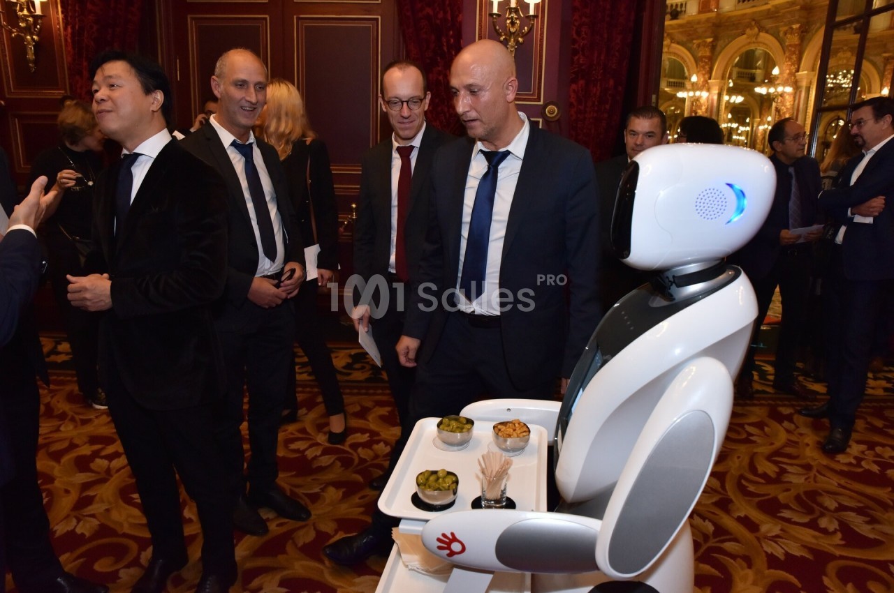 Un robot équipé d'un plateau sert des amuse-bouches à un groupe d'hommes en costume dans un cadre élégant.