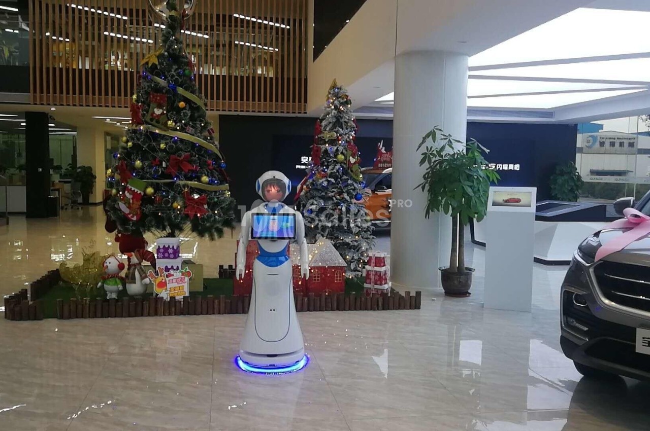 Un robot interactif dans un showroom décoré pour Noël, avec des sapins illuminés et des voitures exposées.
