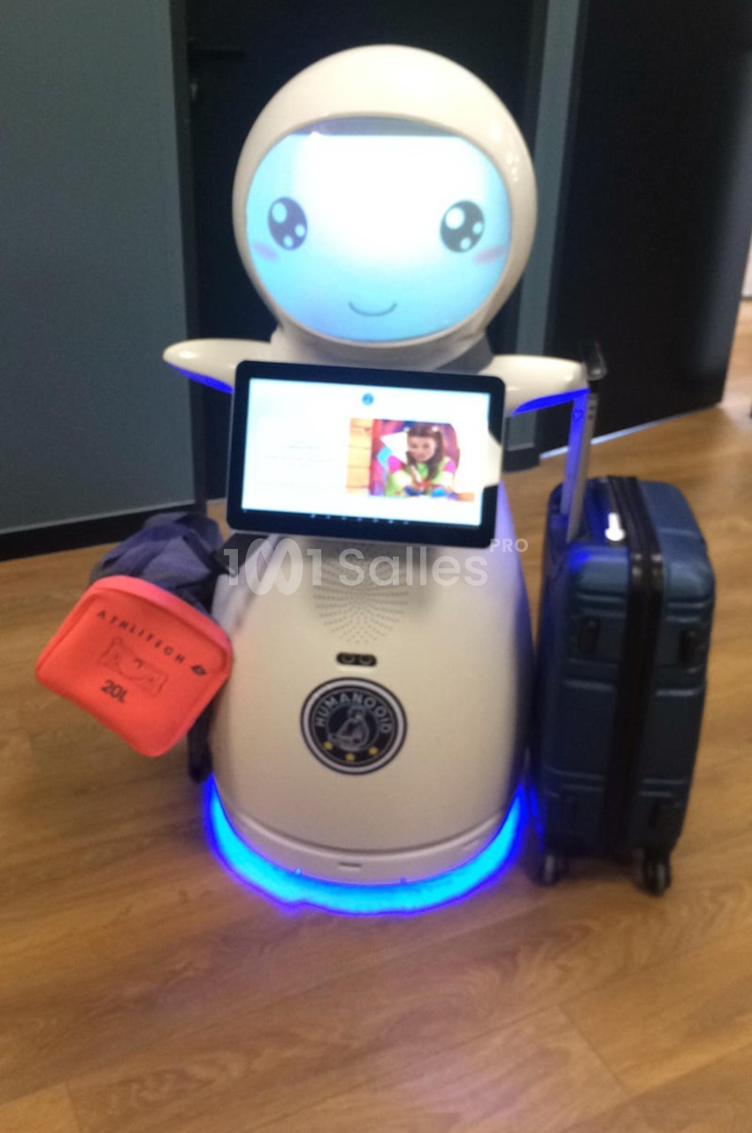 Robot blanc avec un écran affichant une interface, transportant des bagages sur un sol en bois.