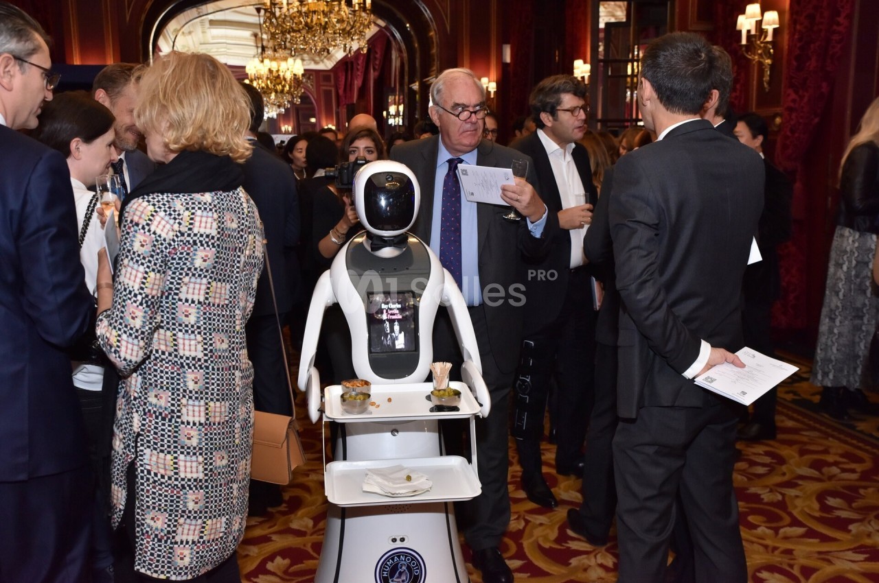Un robot équipé d'un plateau sert des boissons et des amuse-bouches lors d'un événement dans un cadre élégant.