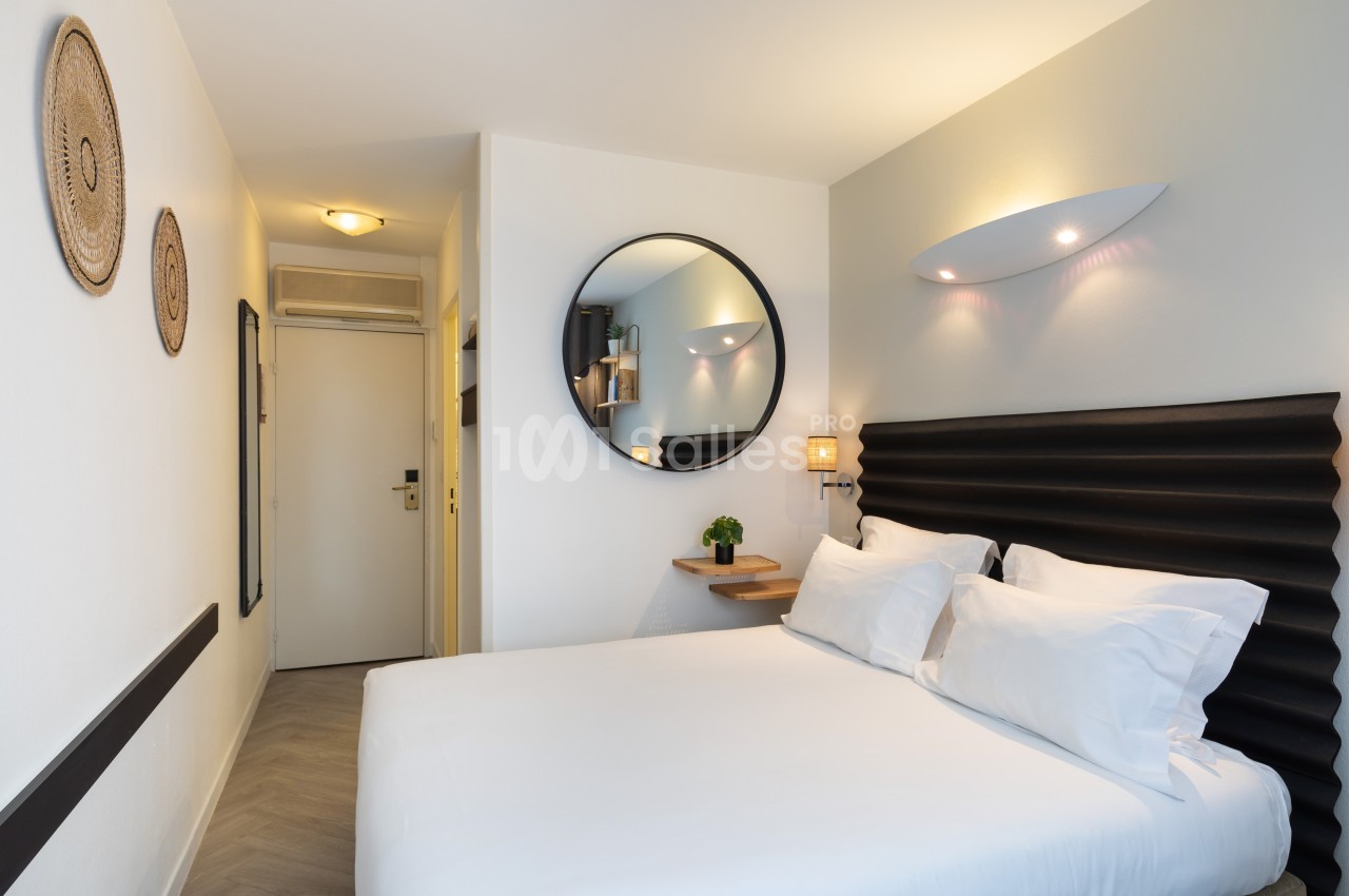 Chambre lumineuse avec un lit double, tête de lit noire, miroir rond, étagères murales et décorations murales.