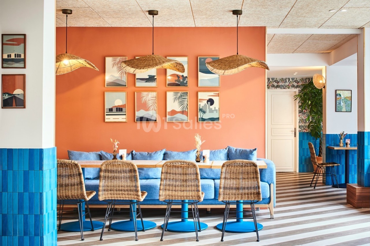 Salle à manger lumineuse avec murs orange, chaises en rotin, table en bois et décorations murales colorées.
