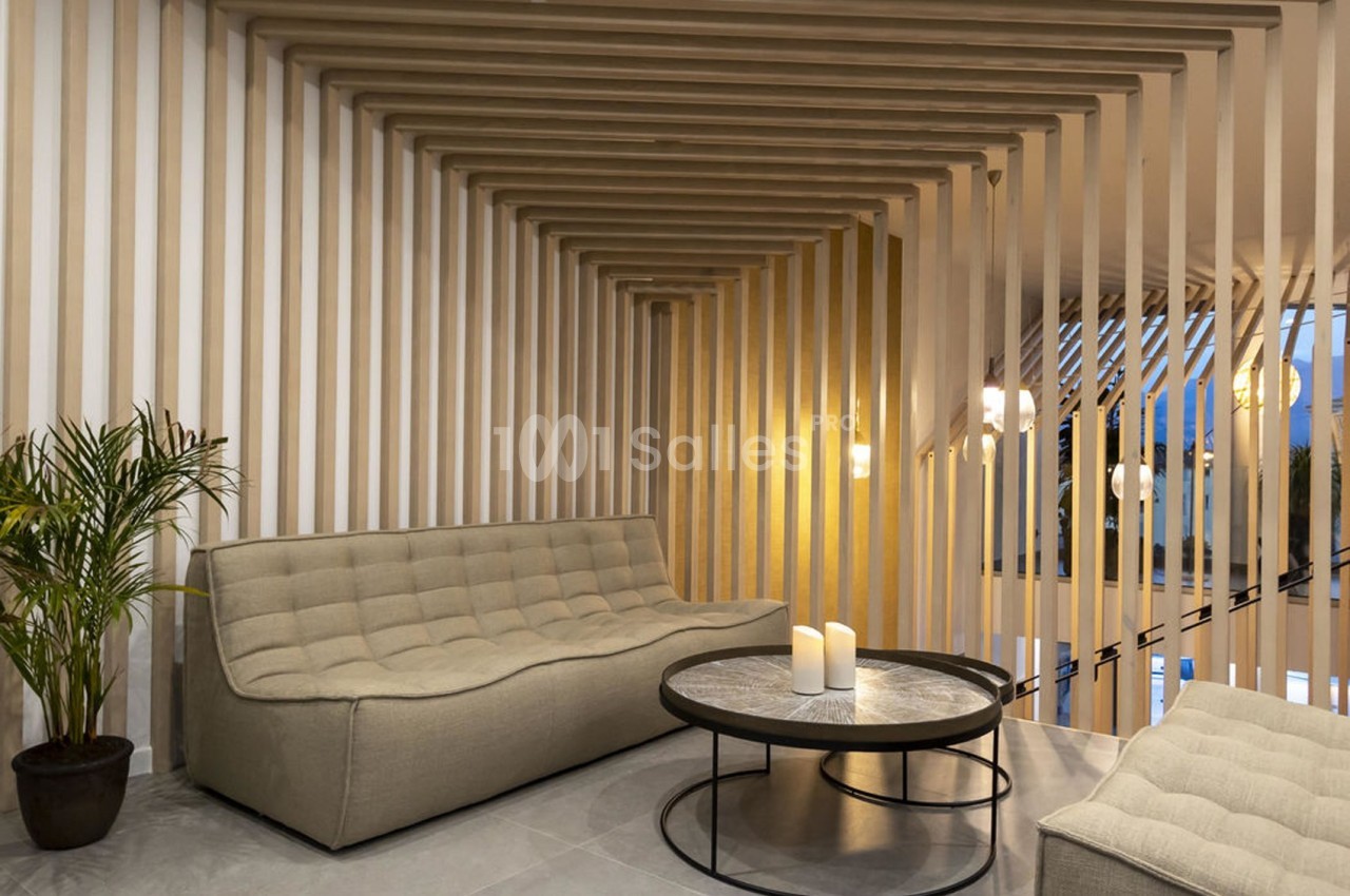 Salon moderne avec canapé beige, table basse ronde en marbre, bougies et décor en bois avec éclairage doux.