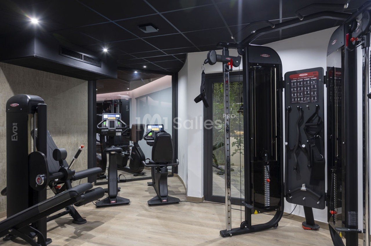 Salle de sport moderne avec équipements de musculation et de cardio, éclairage tamisé et sol en bois.
