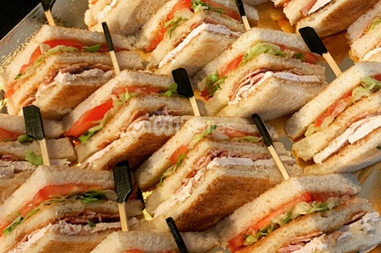 Assortiment de sandwichs club garnis de dinde, tomate, laitue et mayonnaise, maintenus par des pics en bois.