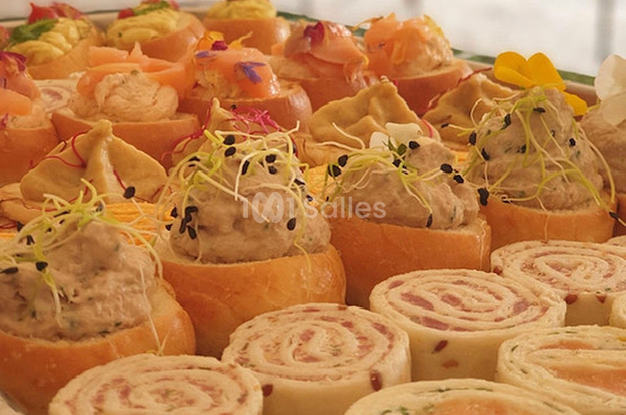Plateau de bouchées apéritives variées, incluant roulés, mini-sandwichs et garnitures colorées.