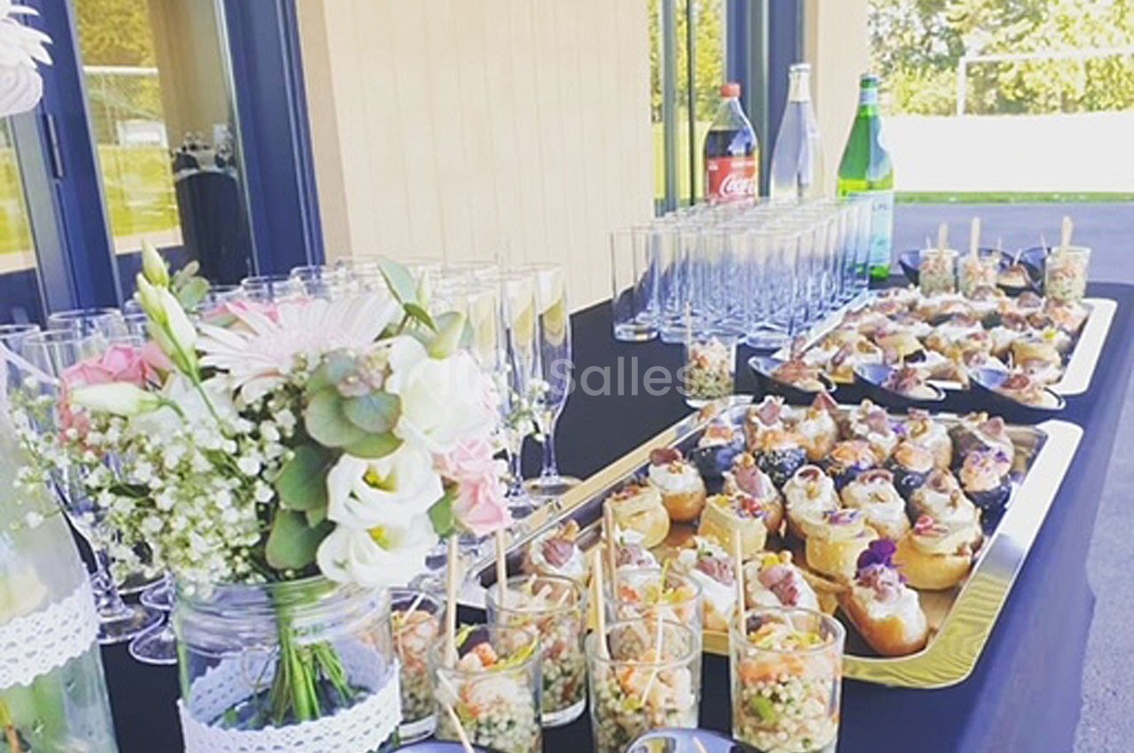 Buffet en extérieur avec verrines, cupcakes et boissons disposés sur une table noire, décorée de fleurs.