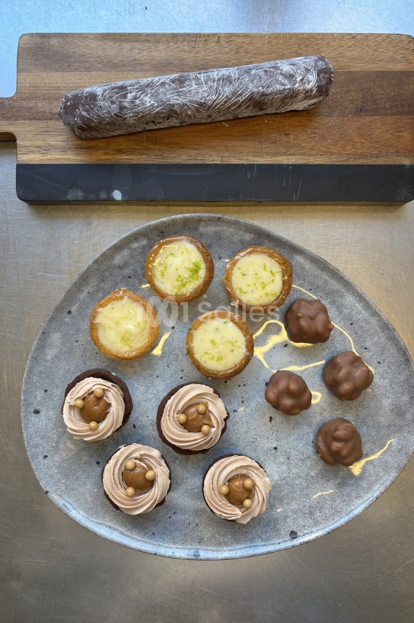 Assortiment de desserts sur une assiette : tartelettes, cupcakes au chocolat et bouchées enrobées, avec un roulé au chocolat.
