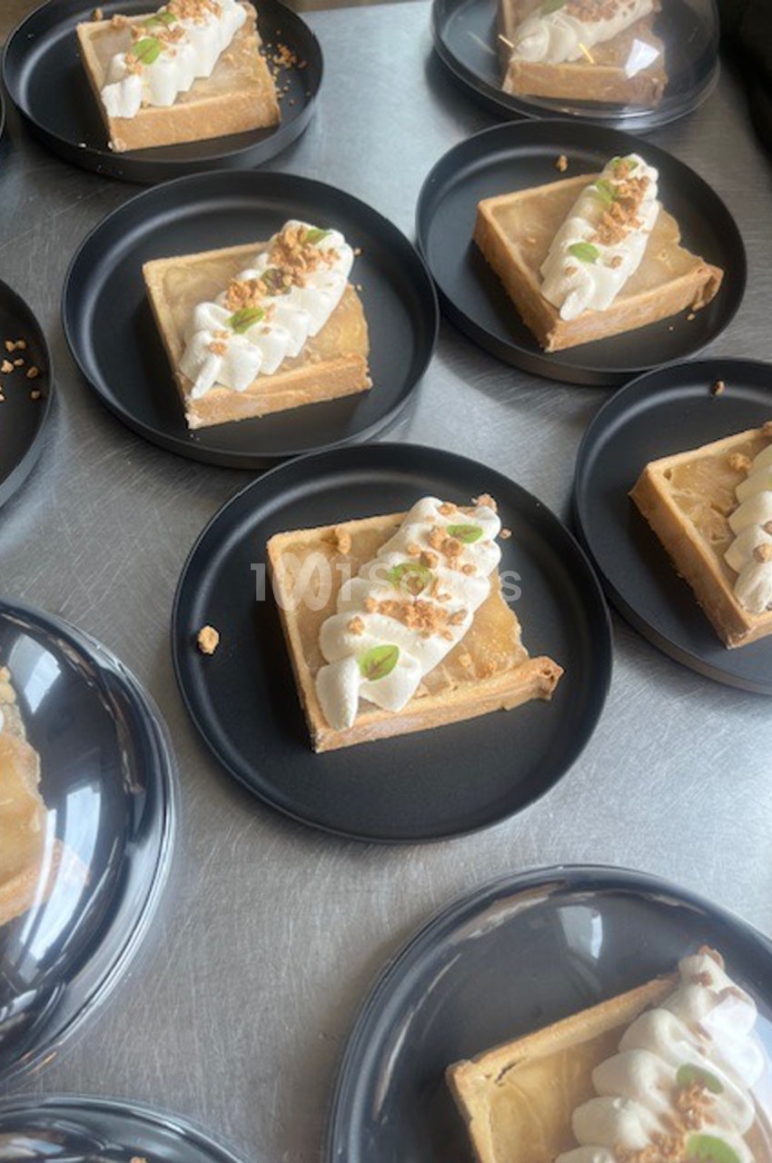 Parts de tarte garnies de crème fouettée, éclats de noix et zestes, présentées sur des assiettes noires.