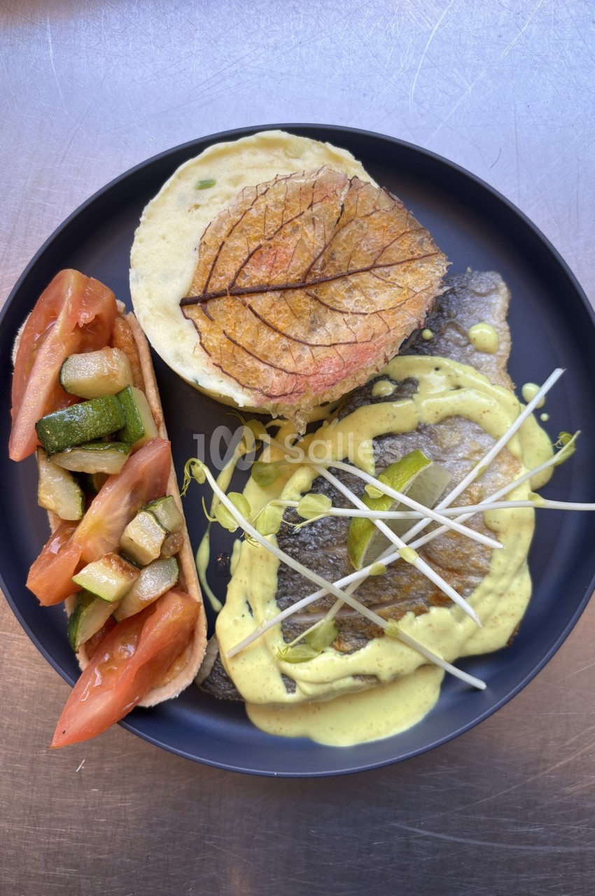Assiette composée de poisson, purée garnie d'une feuille décorative, légumes grillés et sauce crémeuse.