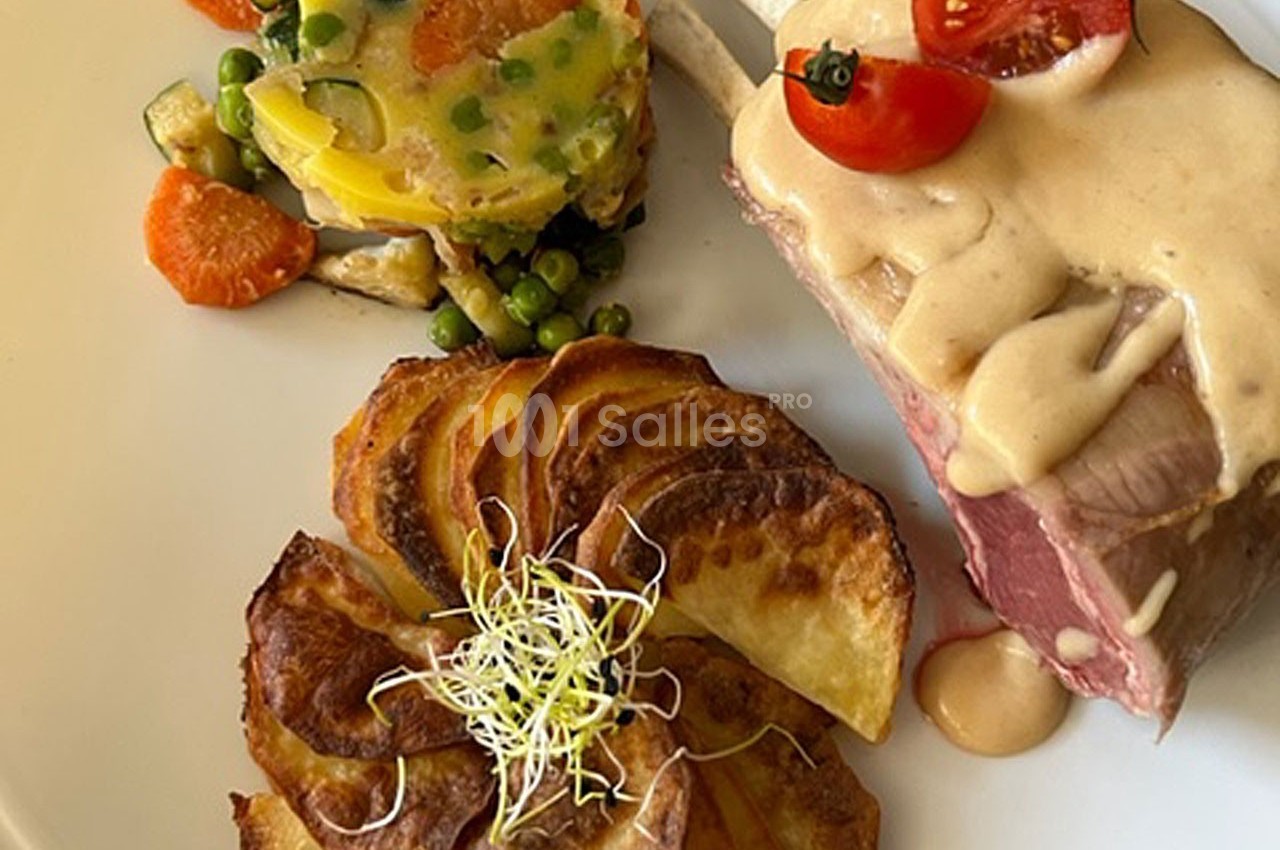 Assiette composée d'un carré d'agneau avec sauce, légumes variés et pommes de terre rôties garnies de pousses.
