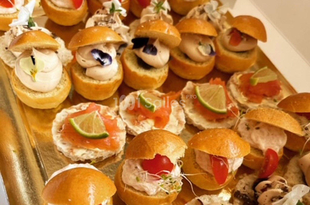 Plateau de mini-sandwichs et canapés garnis de saumon, crème, légumes et herbes sur un plateau doré.