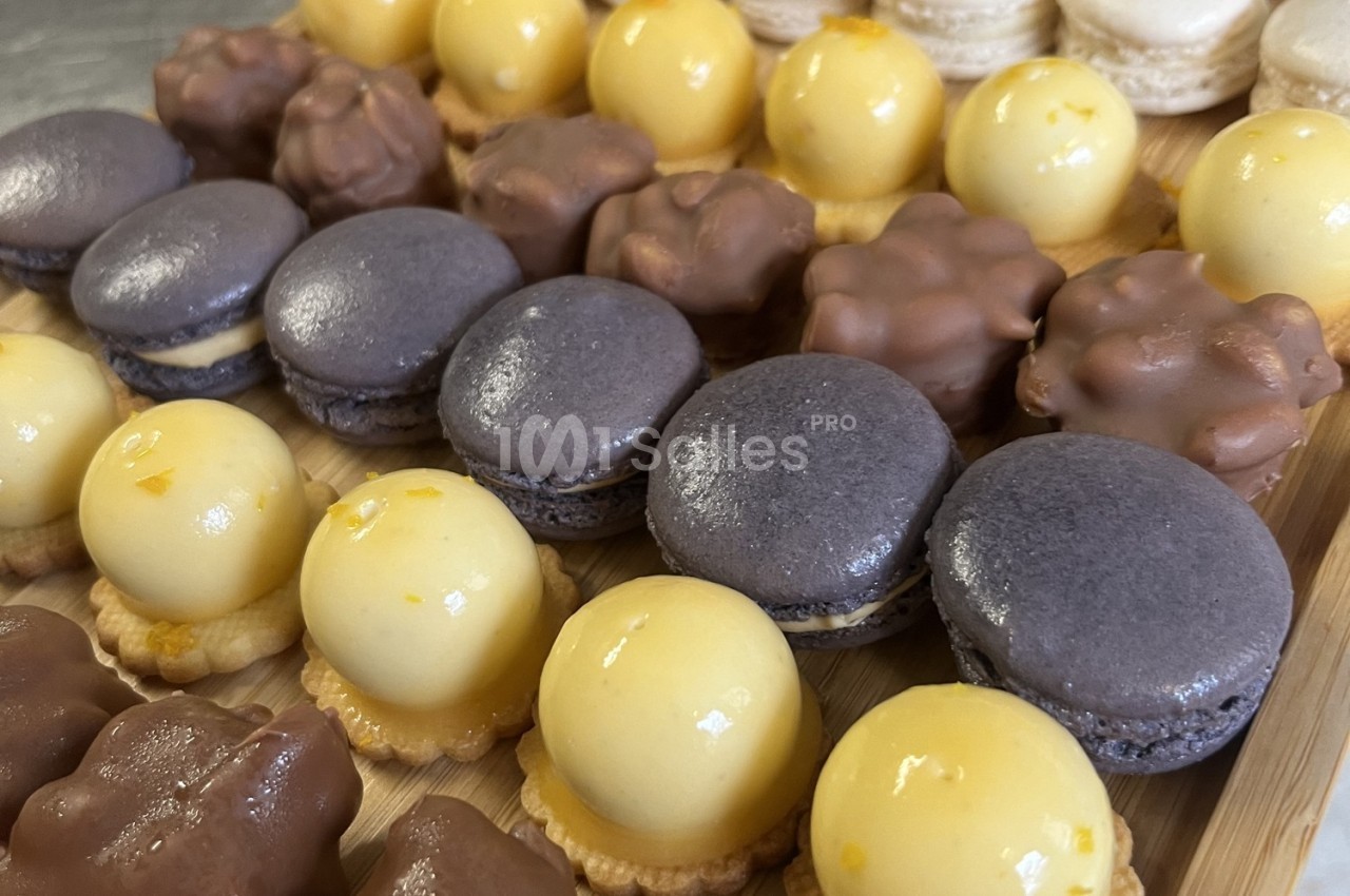 Assortiment de pâtisseries miniatures comprenant macarons violets, tartelettes jaunes et bouchées chocolatées.